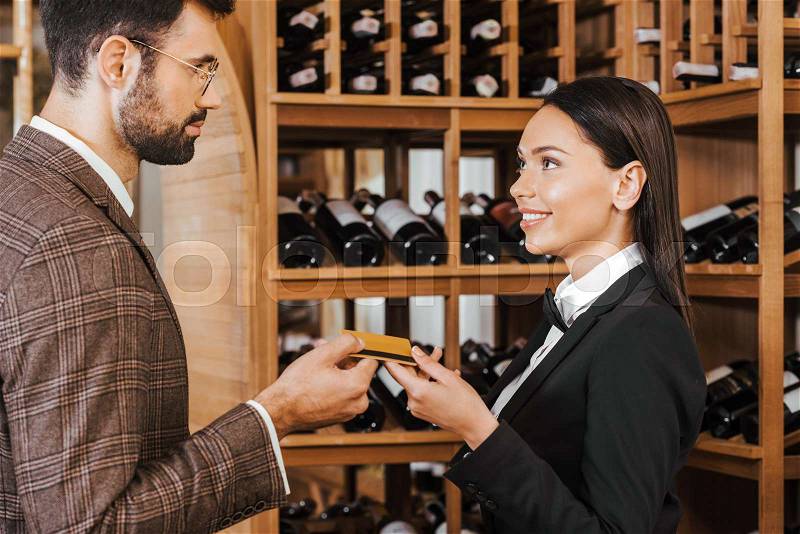 Female wine steward taking credit card from customer at wine store, stock photo