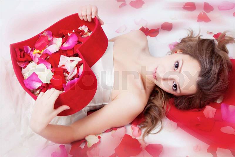 Beautiful girl with rose petals in heart form box, stock photo