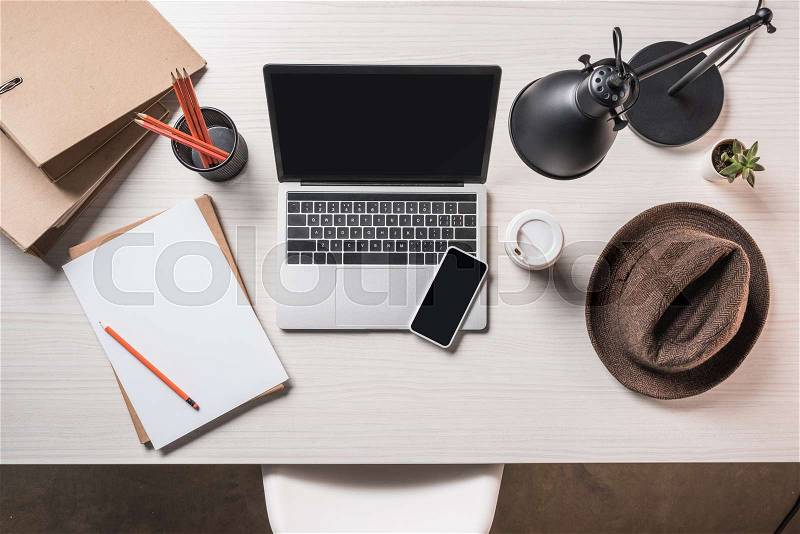 Top view of workplace with fedora hat, coffee cup, empty paper, smartphone and laptop on table , stock photo
