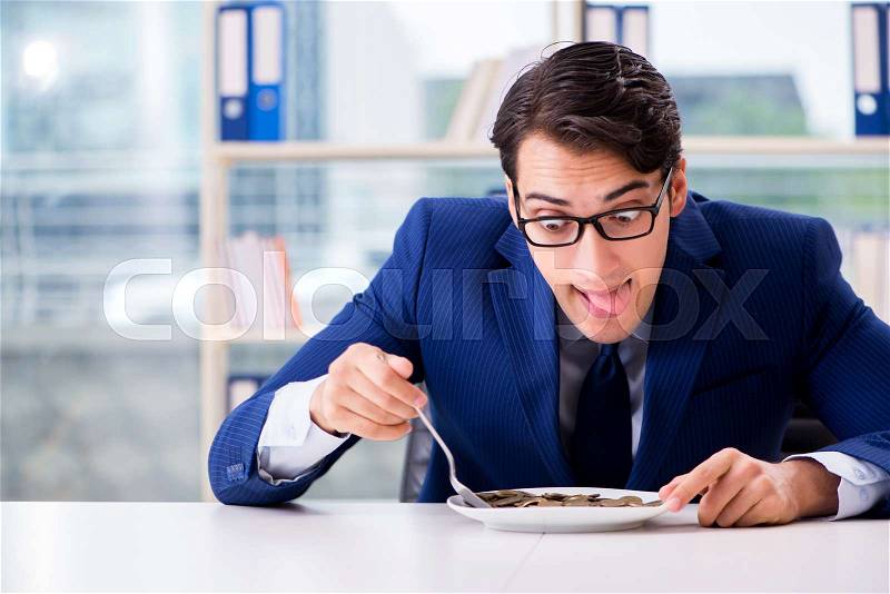 Funny businessman eating gold coins in office, stock photo