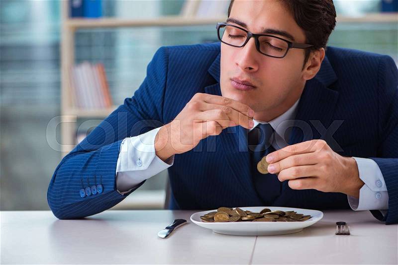 Funny businessman eating gold coins in office, stock photo