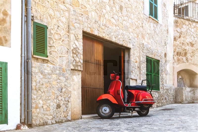 Vintage red motor scooter parked on cobbled street in hostoric spanish village, stock photo