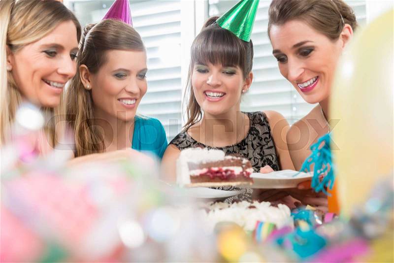 Four beautiful women and best friends smiling while sharing a tasty birthday cake during surprise anniversary at home , stock photo
