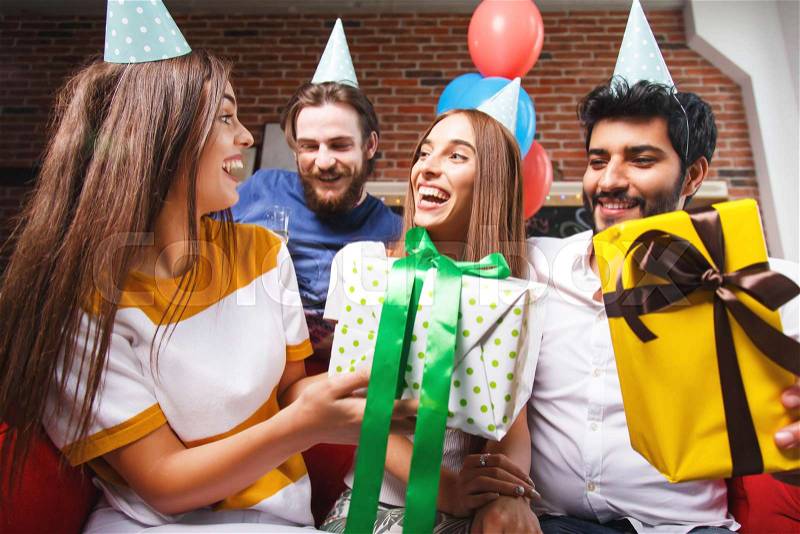 Friends offering gifts to amazing woman in a party hat, they are smiling and laughing a lot, stock photo