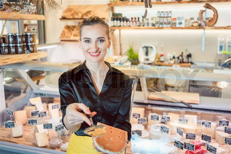 Beautiful woman offering cheese on delicatessen counter cutting a test bit off, stock photo