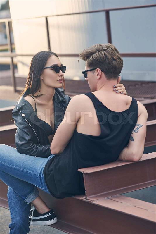 Interracial hot couple in sunglasses hugging and looking at each other on urban roof, stock photo
