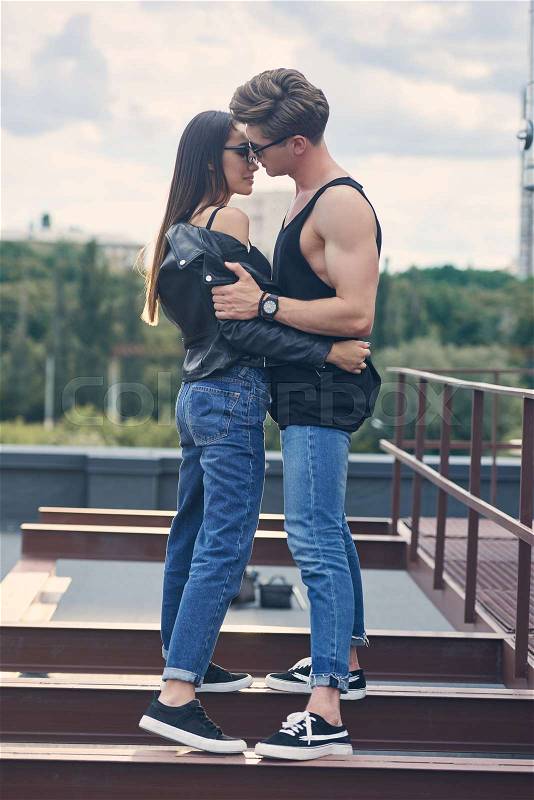 Multiethnic stylish hot couple in sunglasses embracing and going to kiss on urban roof, stock photo