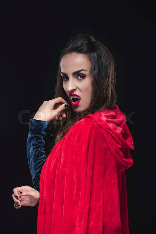 Dreadful vampire woman in red cloak showing her teeth isolated on black, stock photo