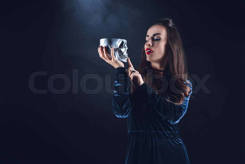 Beautiful vampire holding metal skull on dark background with smoke , stock photo