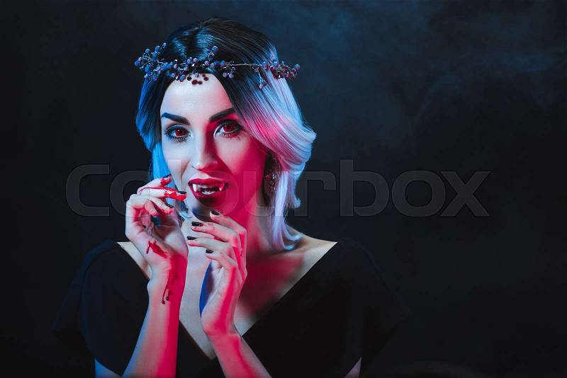 Mystic woman showing vampire teeth on dark background with smoke , stock photo