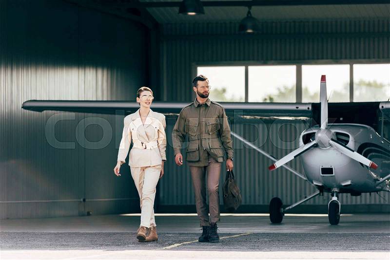 Handsome man carrying bag and walking with stylish girlfriend near hangar with plane , stock photo