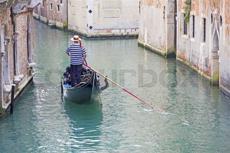 Venetian gondolier in the gondola is transported tourists through canal waters of Venice Italy, stock photo