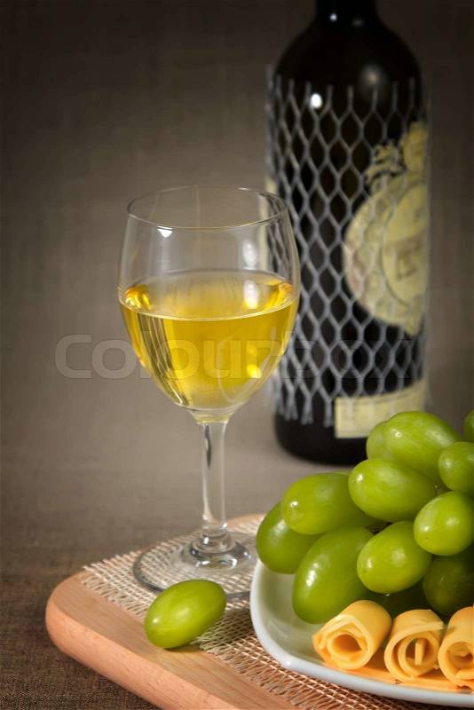 A glass of white wine, green grapes and a bottle of wine on a wooden surface, stock photo