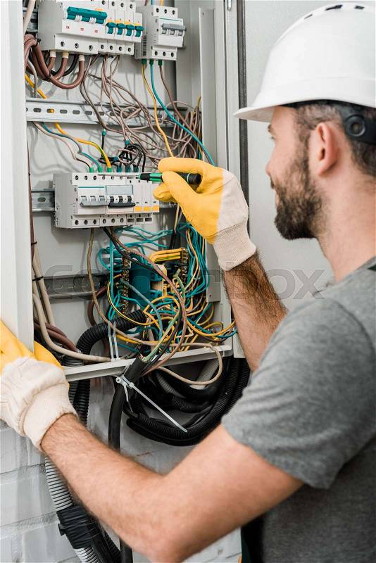 Side view of electrician repairing electrical box and using screwdriver in corridor, stock photo