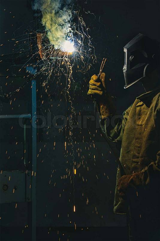 Worker in protection mask welding metal at factory, stock photo