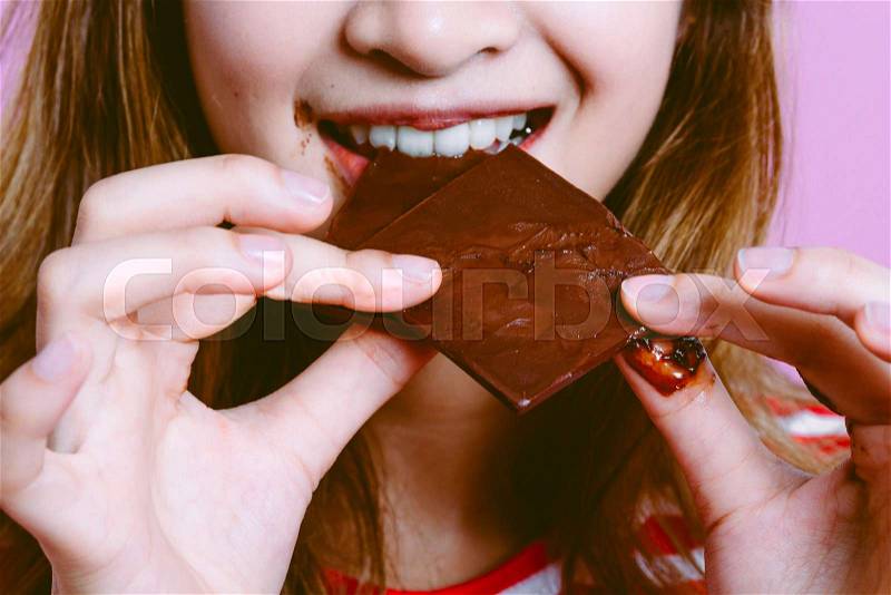 Beautiful woman eating dark chocolate on pink background, stock photo