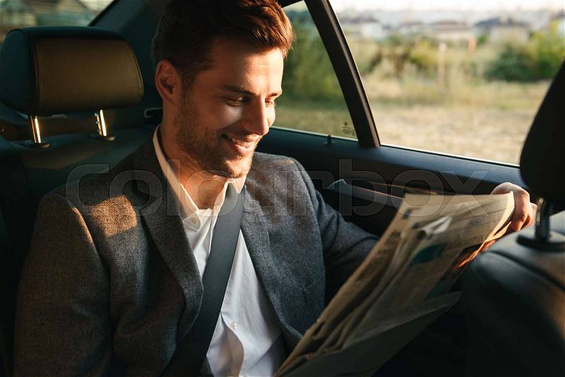Laughing businessman reading newspaper while sitting at the back of a car, stock photo