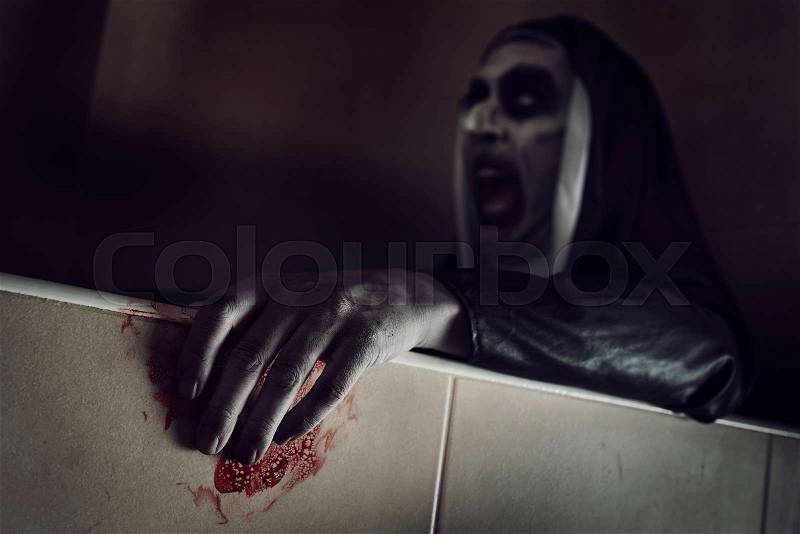 Closeup of a frightening evil nun, wearing a typical black and white habit, with her hands stained with blood, stock photo