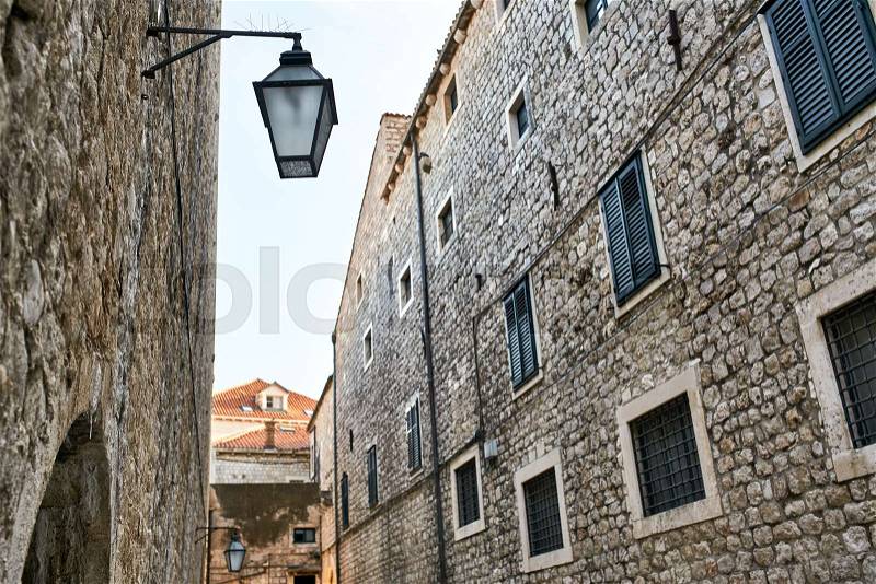 Street with old stone houses with windows with shutters on the blue sky background in Dubrovnik in Croatia. There are hanging vintage lanterns. It is sunny. ..., stock photo