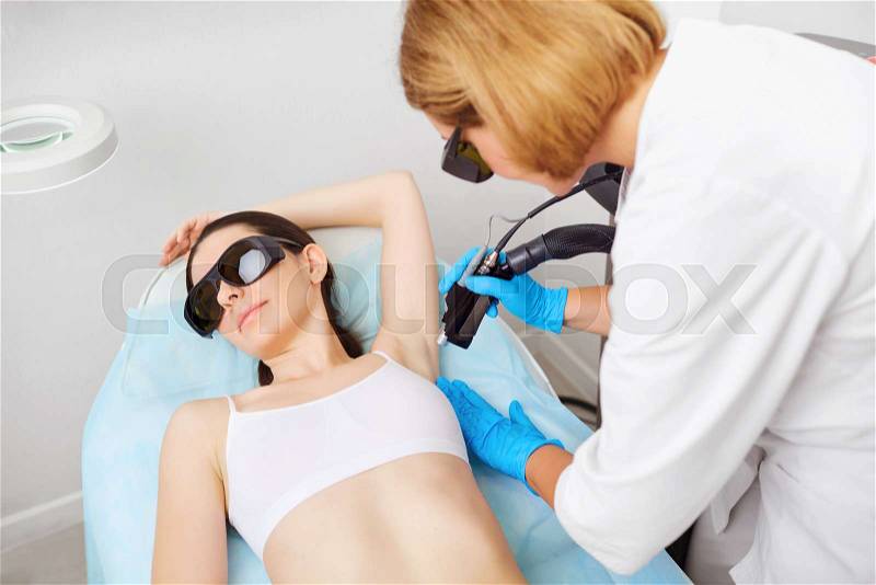 Laser hair removal under the arm of a young woman in a cosmetology clinic. Cosmetlog removes the hair under the arm on the girl\'s hand with a laser, stock photo