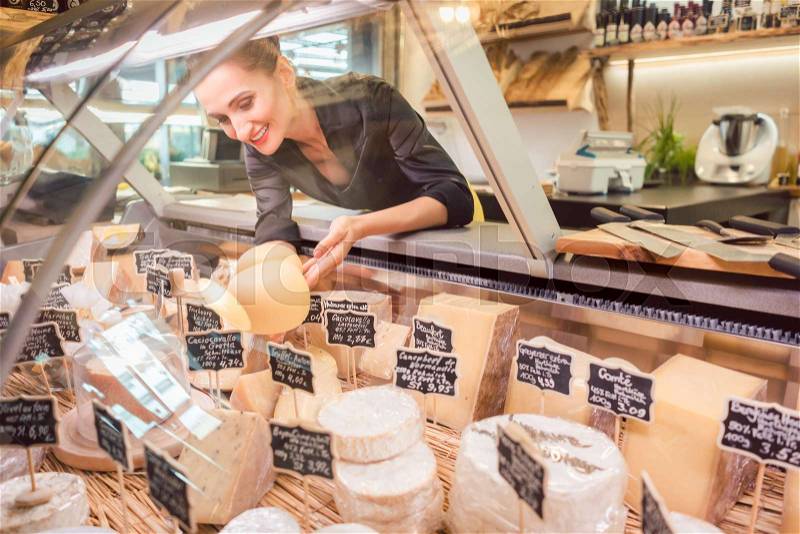Shop clerk woman sorting cheese in the supermarket display to sell it, stock photo