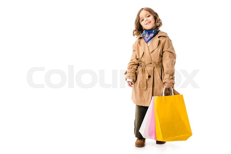 Adorable little child in trench coat with colorful shopping bags looking at camera isolated on white, stock photo