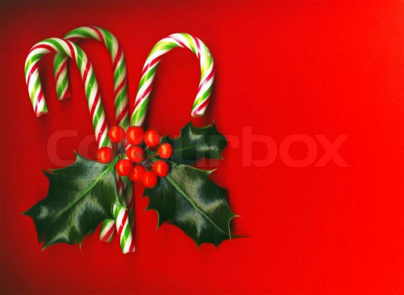 Candy cane with pretty holly leaves and berries on red background, candy cane, stock photo