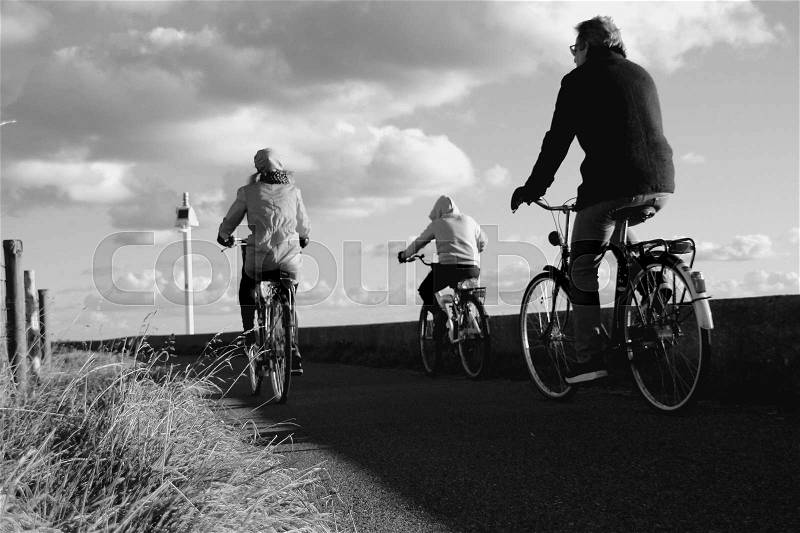 Sky with clouds and a married couple, man and wife are biking with their son on the dyke in the village Zuidland in the beautiful autumn in black and white, stock photo