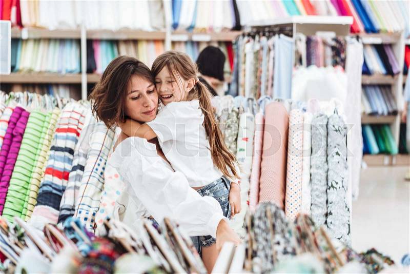 Mom and daughter in the fabric store chooses a multi-colored fabric, stock photo