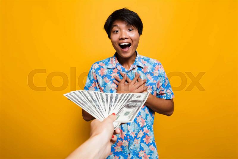 Excited asian man receiving money banknotes isolated over yellow background, stock photo