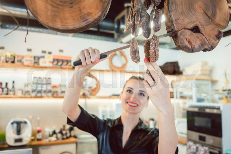 Sales clerk in deli cutting sausages to sell them to customers, stock photo