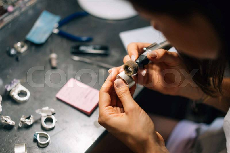 The girl works on a jewelry in the workshop. Jewelry repair shop. Tools, unfinished silverware and rough stones. The girl is a master jeweler, stock photo