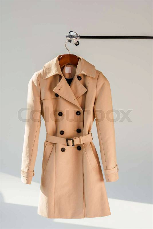 Beige trench coat with belt and black buttons on hanger, stock photo