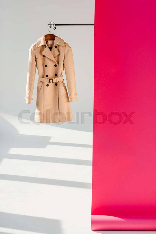 Elegant beige trench coat on hanger with pink wallpaper, stock photo
