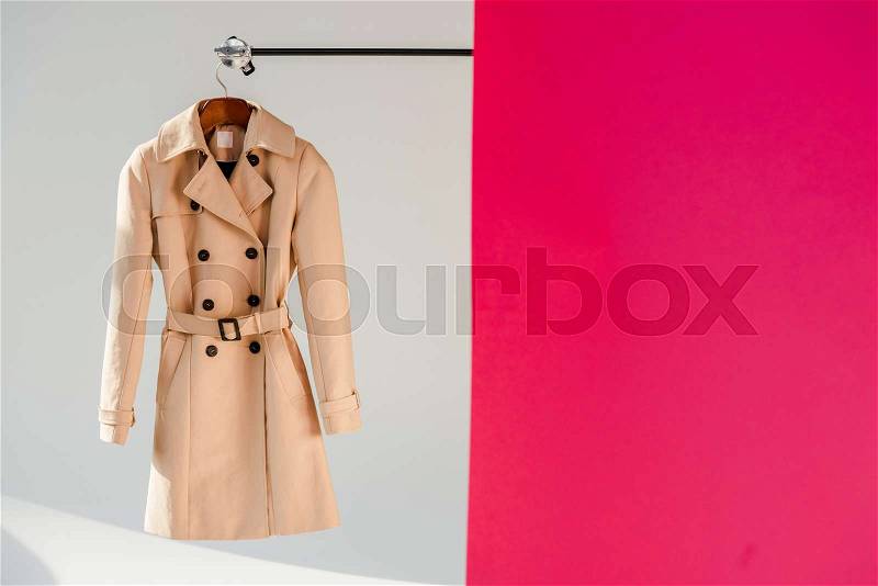 Elegant beige trench coat on hanger at pink and grey background , stock photo