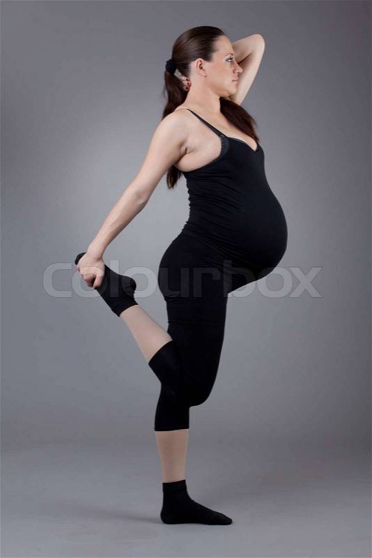 Pregnant woman doing gymnastic exercises on grey background, stock photo
