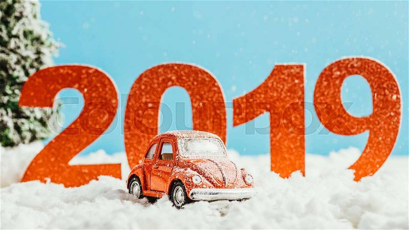 Big red 2019 numbers with toy car standing on snow on blue background, new year concept, stock photo
