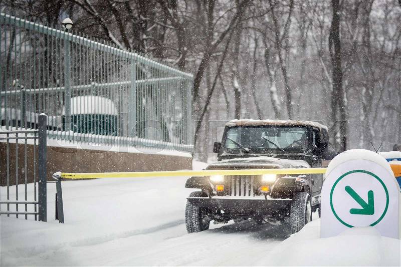 SUV car stopped at automatic entry gate during heavy snowfall. Vehicle access gateway system. Season of Blizzard at winer on city street, stock photo