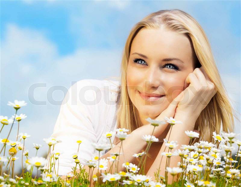 Beautiful woman enjoying daisy field and blue sky, nice female lying down in the meadow of flowers, pretty girl relaxing outdoor, happy young lady and green spring nature in harmony, stock photo