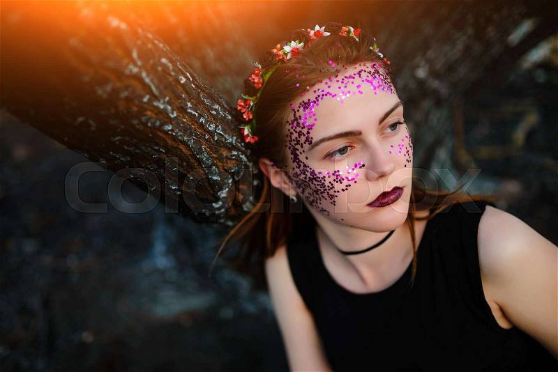 A young beautiful woman with a violet shine on her face stands near a burnt tree, stock photo