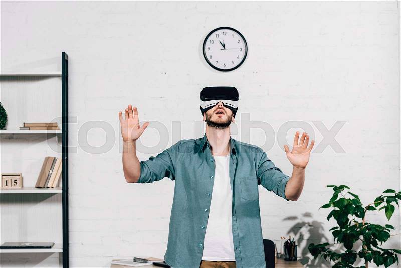 Selective focus of young man with wide arms using virtual reality headset at home, stock photo