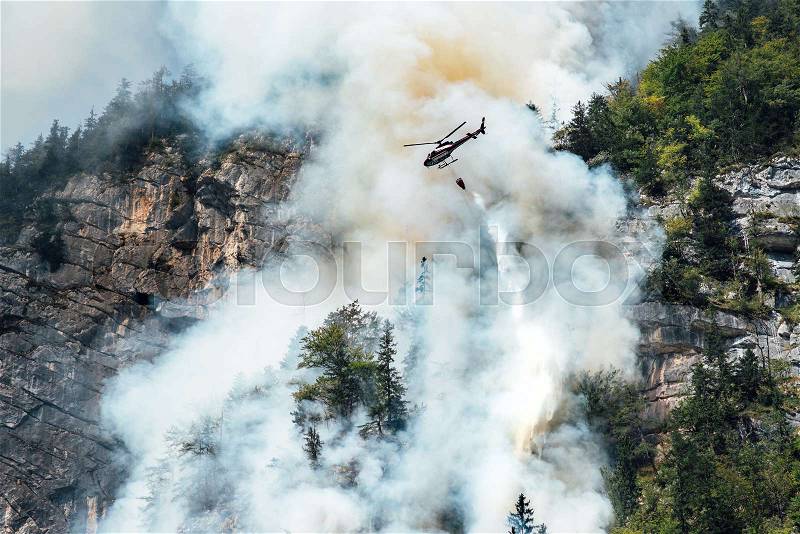 Helicopter extinguishes forest fire on the slope of a fuming mountain, stock photo