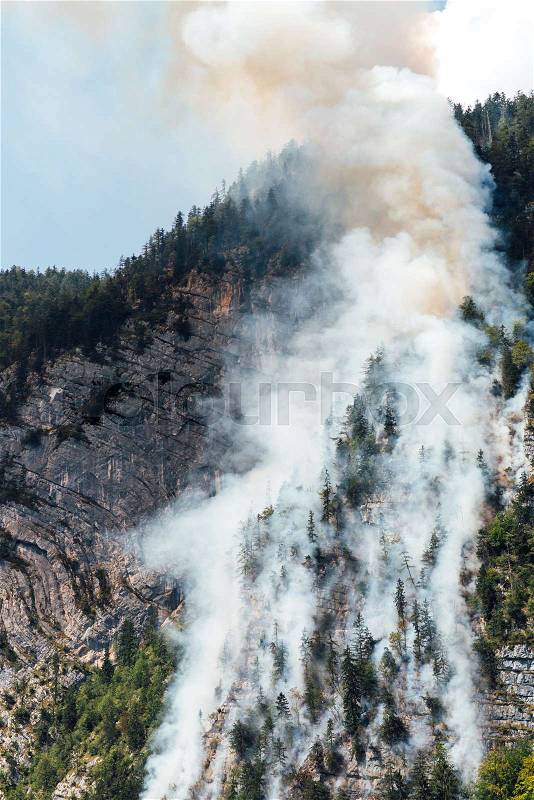 Helicopter extinguishes forest fire on the slope of a fuming mountain, stock photo