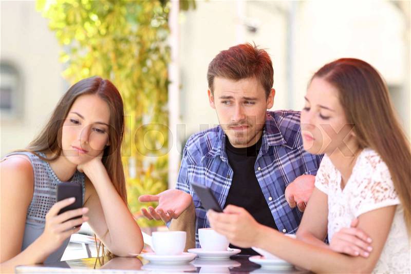 Man being ignored by his friends who are using their smart phones, stock photo