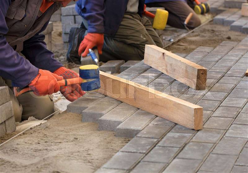The workers lay the paving slab with special hammers, leveling it according to the level of the tensioned thread, stock photo