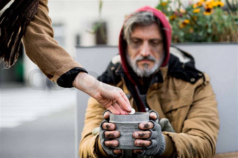 Unrecognizable woman giving money to homeless beggar man sitting outdoors in city, stock photo