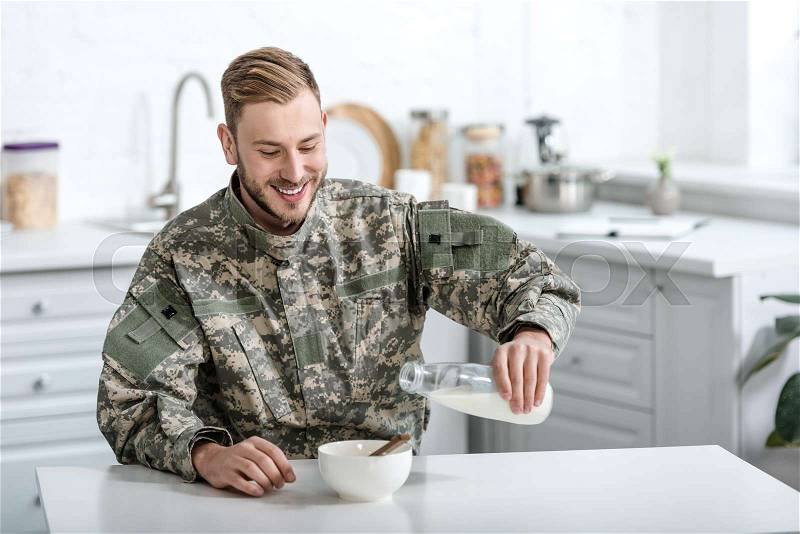 Smiling military man pouring milk in bowl with cornflakes , stock photo