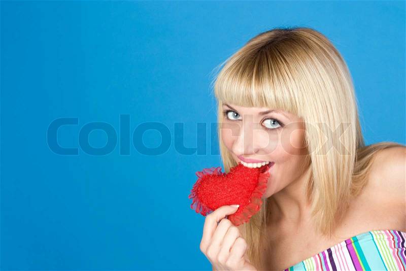 Attractive woman biting a red heart over blue background, stock photo