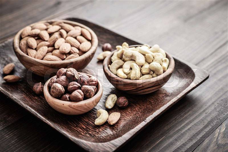 Almonds, cashew and hazelnuts in wooden bowls on wooden background, stock photo
