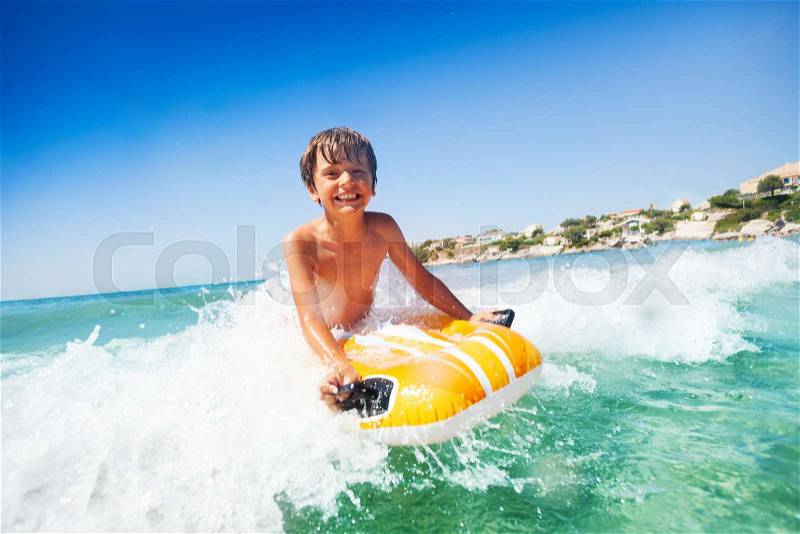 Portrait of joyful boy riding the waves on swimming mattress during summer vacation, stock photo